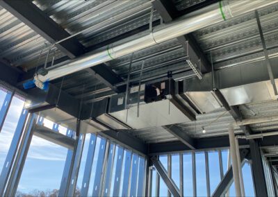 Interior of a building under construction showing exposed steel beams and air ducts against a blue sky.
