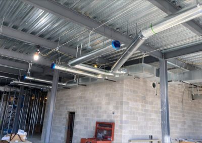 Interior of a construction site with exposed ductwork, wiring, and a worker in the background.