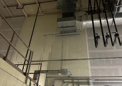 Overhead view of industrial piping and ductwork against a ceiling in a commercial building.